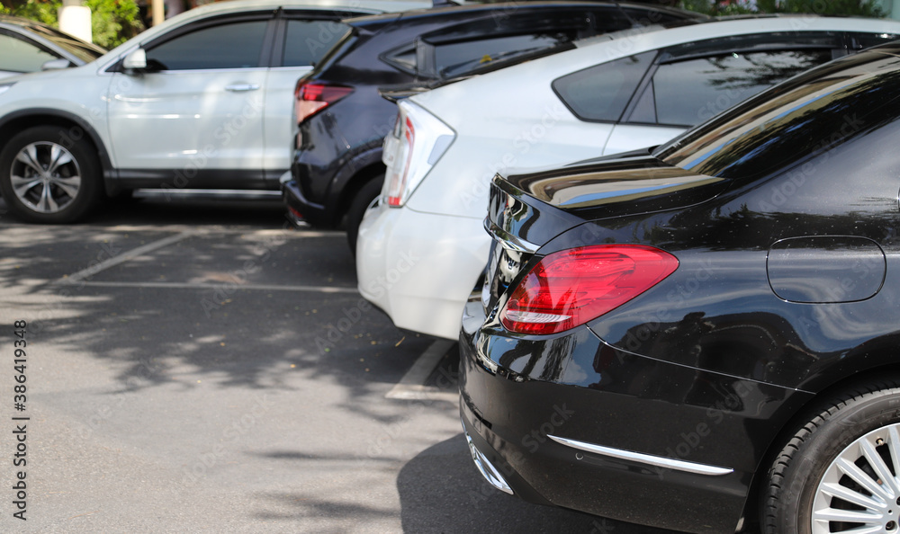 Closeup of rear, back side of black car with  other cars parking in parking area in bright sunny day. 