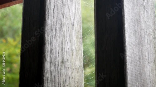 Raining weather in rural mountain countryside through rustic oak wood barn beams window with spider web dolly right photo