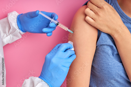 close up of doctor hand using syringe to make vaccine injection to young adult female patient  isolated on pink background