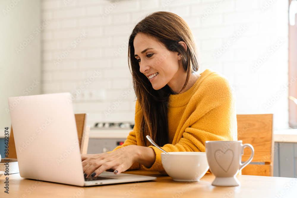 Beautiful woman using laptop computer while having breakfast at home