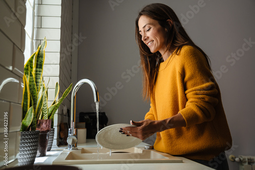Fotografie Beautiful middle-aged woman smiling while washing dishes at home