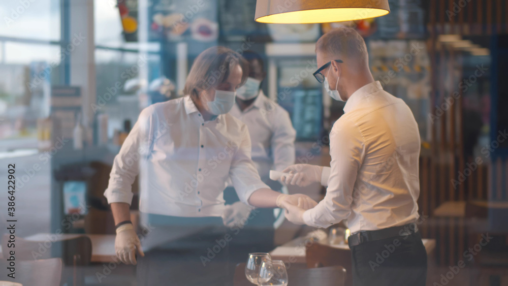 View through window of cafe owner measuring temperature of waiters with infrared thermometer View through window of cafe owner measuring temperature of waiters with infrared thermometer