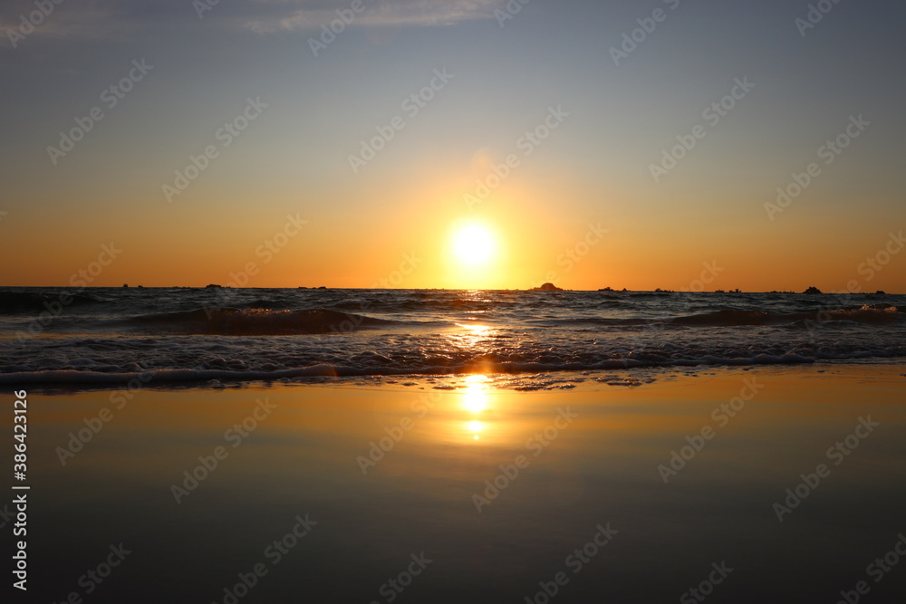 A stunning, orange sunset in the summer at cobo beach on Guernsey. Sun is reflected in the smooth, wet sand.
