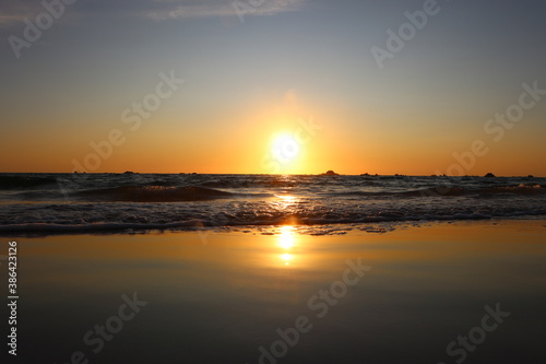 A stunning, orange sunset in the summer at cobo beach on Guernsey. Sun is reflected in the smooth, wet sand.