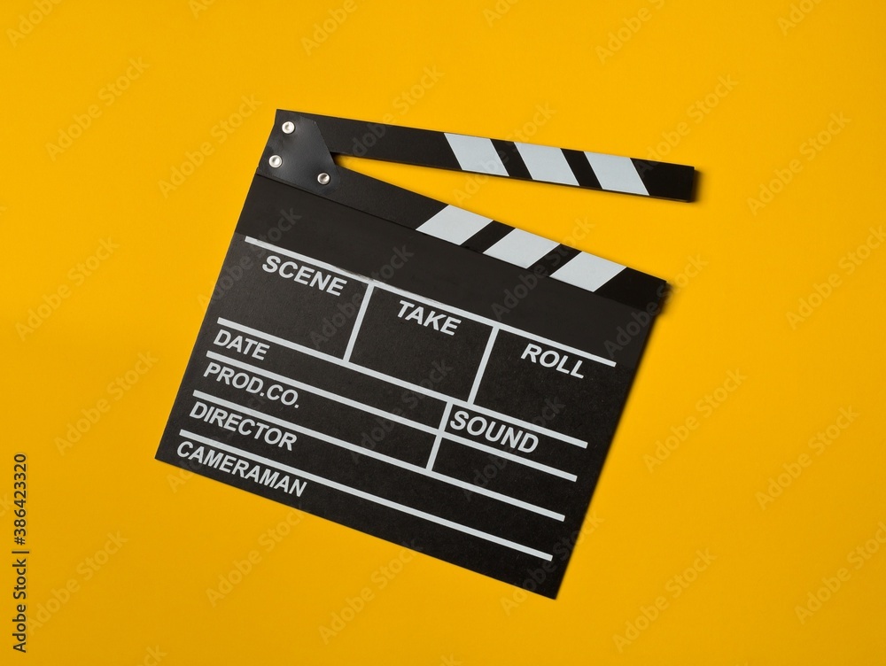 Single, black, opened movie clapper or clapper-board flat lay top down view from above on yellow or orange