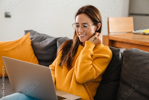 Beautiful caucasian pleased woman smiling and using laptop in apartment