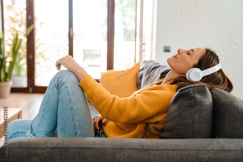 Happy woman listening to music in headphones on sofa at home © Drobot Dean