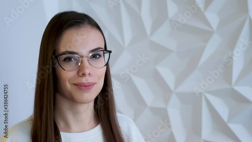 A beautiful brunette girl in white as a doctor cute smiles and rejoices, on a volumetric white geometric background