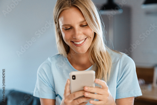 Beautiful joyful caucasian girl using cellphone and smiling at home