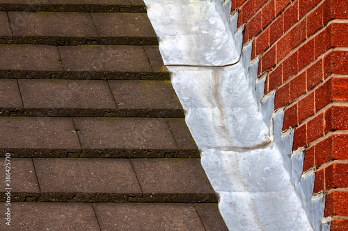 Stepped lead flashing roof gulley creating a water tight seal between roof tiles and brick wall on a domestic house