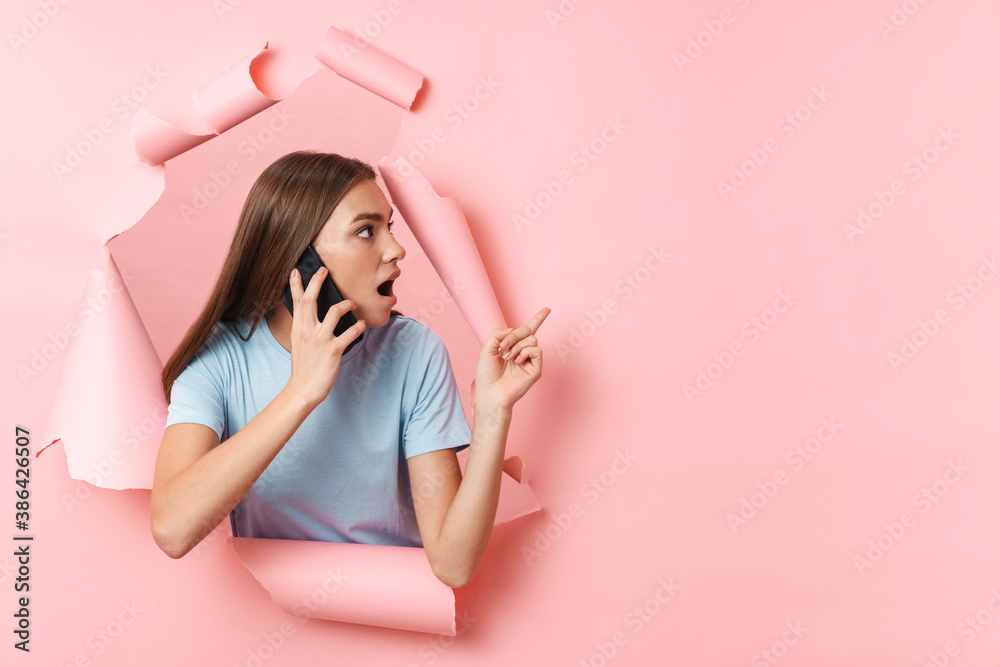 Young brunette woman talking on cellphone and pointing at copyspace Young brunette woman talking on cellphone and pointing at copyspace