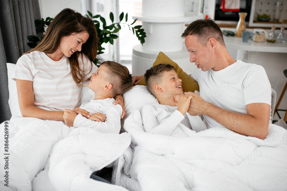 Young family enjoying in bed. Happy parents with sons relaxing in bed.