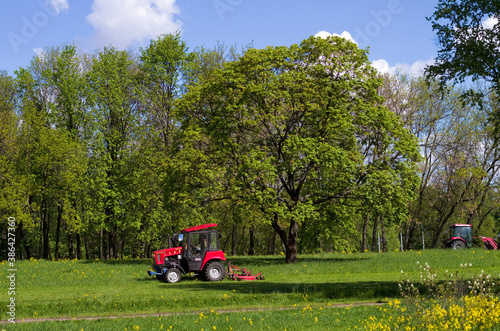 Lawn mover in the park. Red tractor  green grass and trees. Saint-Petersburg  Russia
