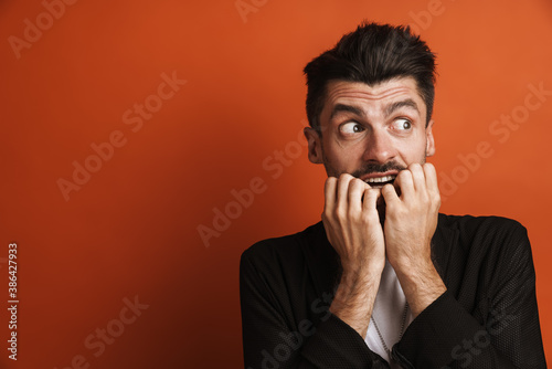 Photo of young frightened man biting his nails at camera