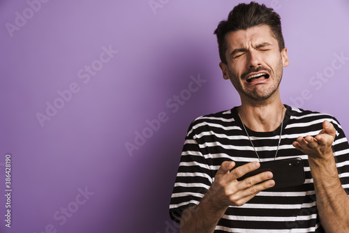 Slika na platnu Photo of unhappy man crying while playing video game on cellphone
