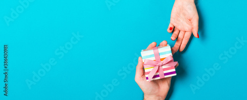 Top view of a man holding and giving a gift to a woman on colorful background. Receiving a present. Close up of holiday concept