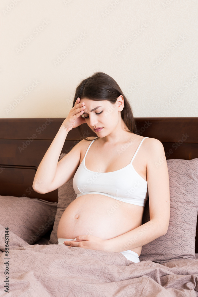 Young pretty pregnant woman suffering from headache at home in bed