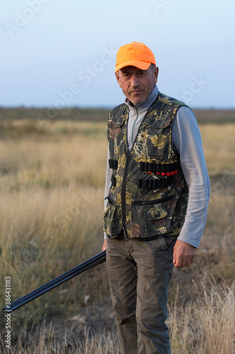 Pheasant hunter with shotgun walking through a meadow.