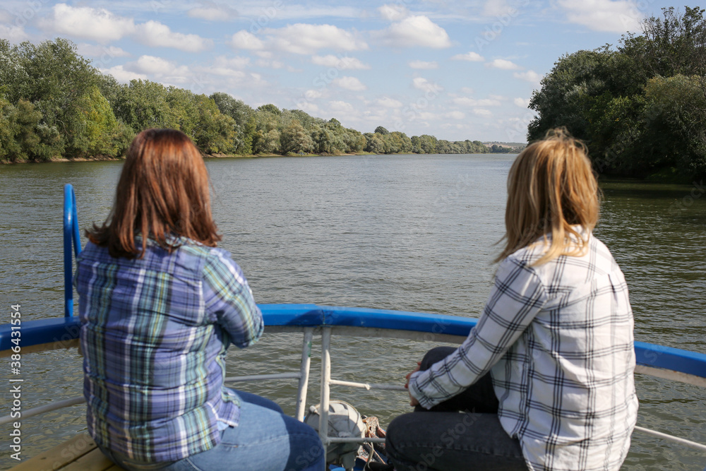 Fototapeta premium Two women sit back on bow of yacht and look at the river. Lesbians ride on a riverboat.