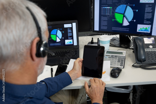 Senior businessman wearing headset holding digital tablet at modern office