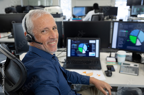 Portrait of senior businessman wearing headset sitting on his desk at modern office