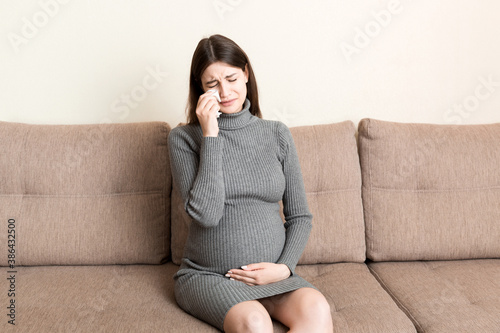 Young vomiting woman sitting on sofa and suffering with nausea. Pregnancy expectation concept, copy space