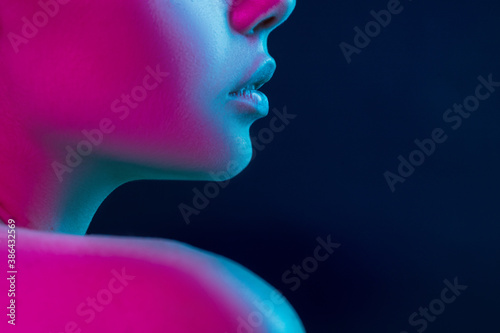Neck and lips. Close up portrait of female fashion model in neon light on dark studio background. Beautiful caucasian woman with trendy make-up and well-kept skin. Vivid style, beauty concept