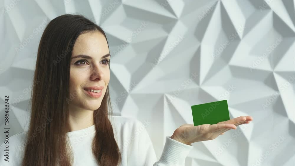 Beautiful brunette girl smiles and shows an element for advertising, with a green screen, on a white volumetric background Beautiful brunette girl smiles and shows an element for advertising, with a green screen, on a white volumetric background