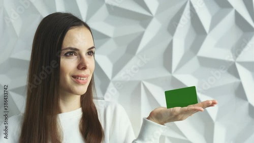 Beautiful brunette girl smiles and shows an element for advertising, with a green screen, on a white volumetric background