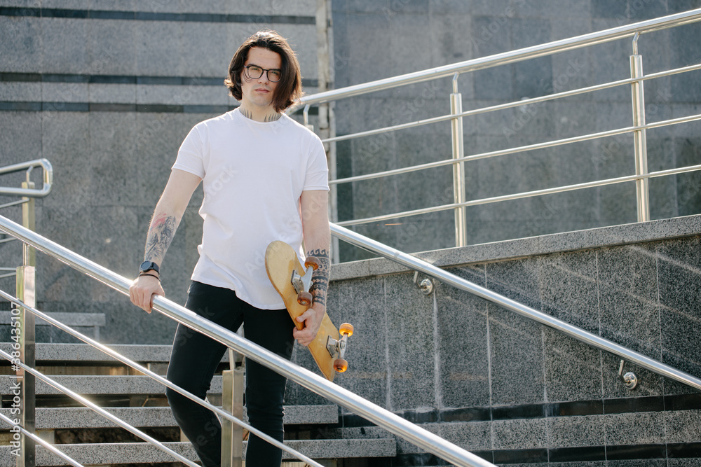 Hipster handsome male model with glasses wearing white blank t-shirt and black jeans with space for your logo or design in casual urban style Hipster handsome male model with glasses wearing white blank t-shirt and black jeans with space for your logo or design in casual urban style