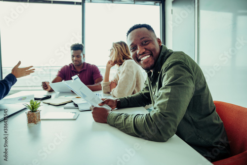 Mixed race business man smiling working through paperwork with parters sitting around table in conference room  photo