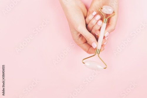 Jade roller in pink in woman hands with perfect manicure. Home skincare tool  trendy beauty device.