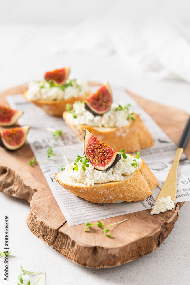 Fresh bread with figs, ricotta, honey and microgreen on a wooden cutting board on white background. Italian Bruschettas with figs. Close up, side view. Cookbook recipe, menu. Fresh bread with figs, ricotta, honey and microgreen on a wooden cutting board on white background. Italian Bruschettas with figs. Close up, side view. Cookbook recipe, menu.