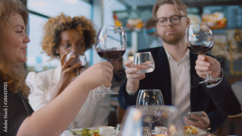 Man with glass of water cheers with diverse friends drinking red wine at bar restaurant
