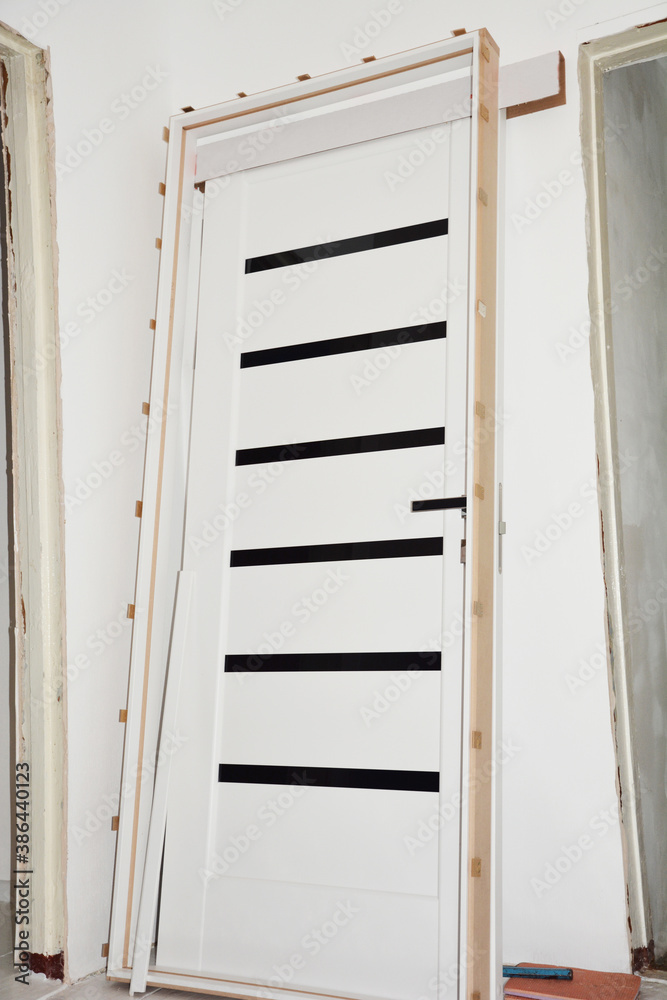 An unpacked black and white laminate interior door with a door handle is going to be installed in a room during the house renovation. An unpacked black and white laminate interior door with a door handle is going to be installed in a room during the house renovation.