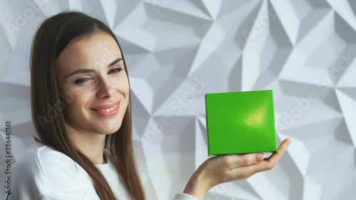 Beautiful brunette girl in white as a doctor holds and demonstrates a box for advertising a product, a green screen for demonstrating a product