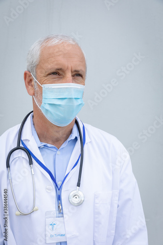 Senior male doctor wearing face mask against grey background