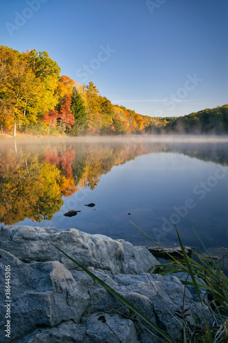 Fototapeta Naklejka Na Ścianę i Meble -  Rose lake at hocking hills state park in ohio during fall. Colorful leaves reflect off the misty water during golden hour light at sunrise. Beautiful fall scene on Ohio lake during autumn