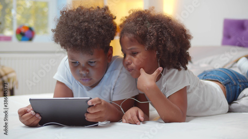 Portrait of adorable african boy and girl kids watching cartoon in earphones on digital tablet