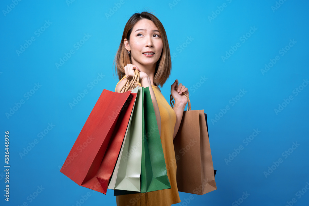 Happy asian beautiful woman holding a shopping bag on it and a credit card, Isolated on a blue background. Happy asian beautiful woman holding a shopping bag on it and a credit card, Isolated on a blue background.