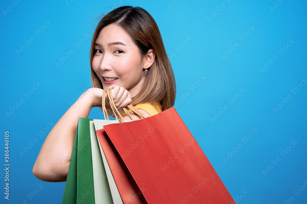 Happy asian beautiful woman holding a shopping bag on it and a credit card, Isolated on a blue background.
