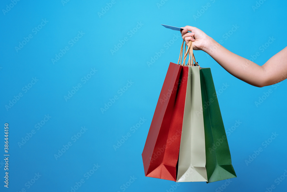 Young woman's hand holding shopping bags and credit card isolated on blue background.