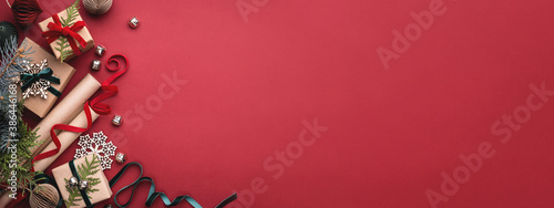 Banner with Christmas gift boxes, velvet ribbons, rolls of wrapping paper and decorations on red background.