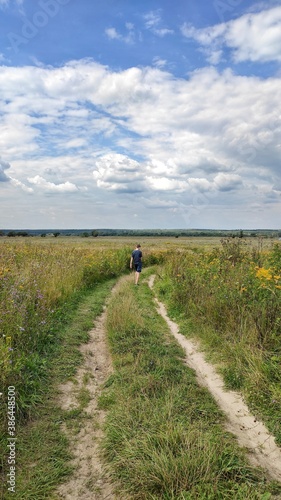 a man walks along a dirt road in a field. 