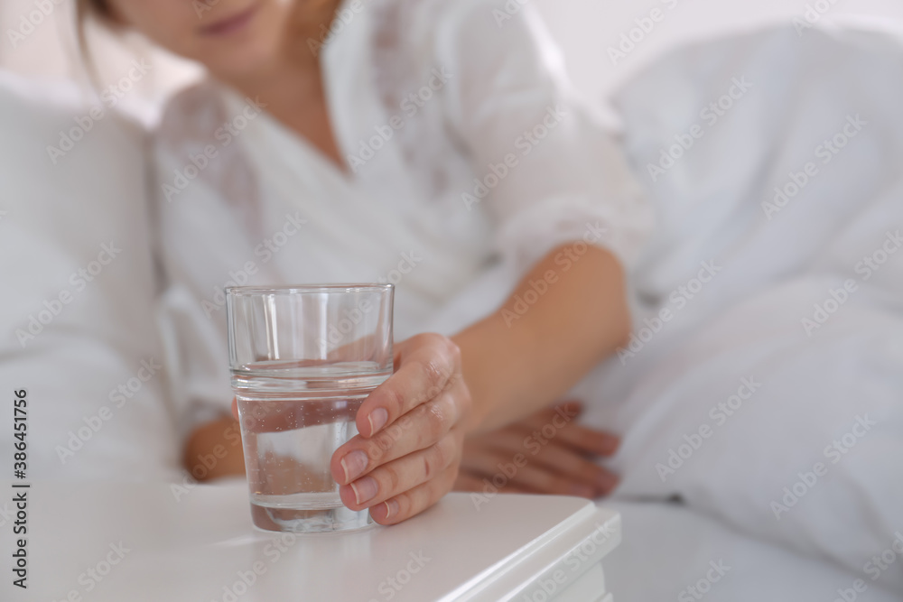 Woman taking glass of water from nightstand in bedroom, closeup Woman taking glass of water from nightstand in bedroom, closeup