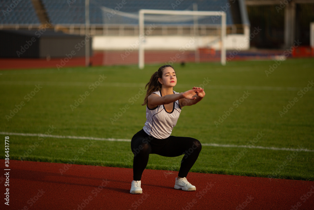 Fitness Girl Doing Workout On Yoga Mat At Outdoor Stadium. Fit Woman With Strong Muscular Body Doing back stretches Exercise Against stadium background. Active Lifestyle For Urban People Fitness Girl Doing Workout On Yoga Mat At Outdoor Stadium. Fit Woman With Strong Muscular Body Doing back stretches Exercise Against stadium background. Active Lifestyle For Urban People