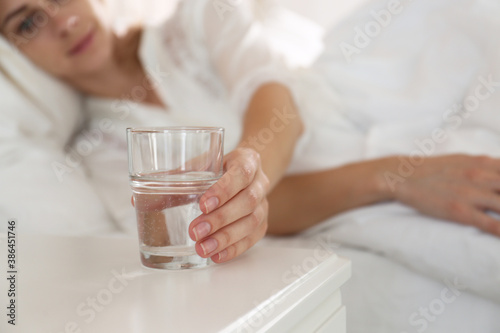 Woman taking glass of water from nightstand in bedroom, closeup