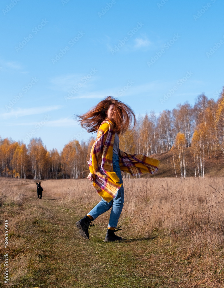 red-haired girl with a dog runs through the autumn forest