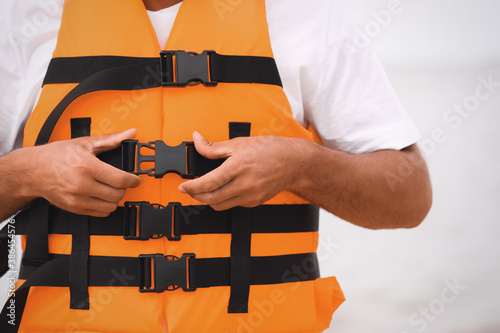 Male lifeguard putting on life vest near sea, closeup