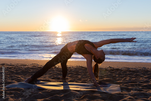 young caucasian woman doing stretches and yoga exercises on the beach on sun rising. photo